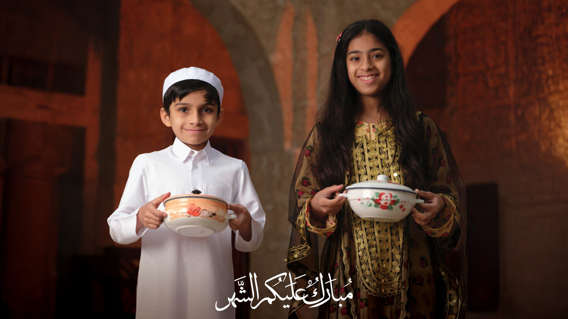 طفل وطفلة يحملان الطعام ويرتديان الزي القطري التقليدي في شهر رمضان